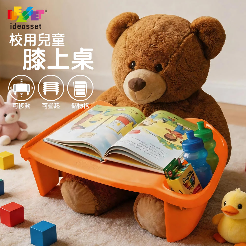 An orange plastic lap desk with a built-in tray, shown with a large brown teddy bear sitting behind it on a carpeted floor. The desk holds an open book and small colorful items in its cup holder.
